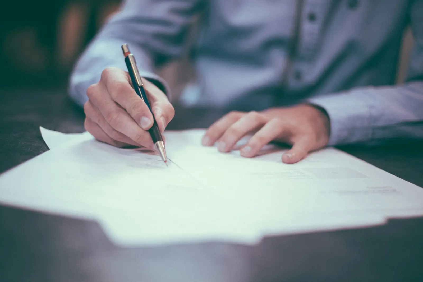 A hand signing paperwork on a desk
